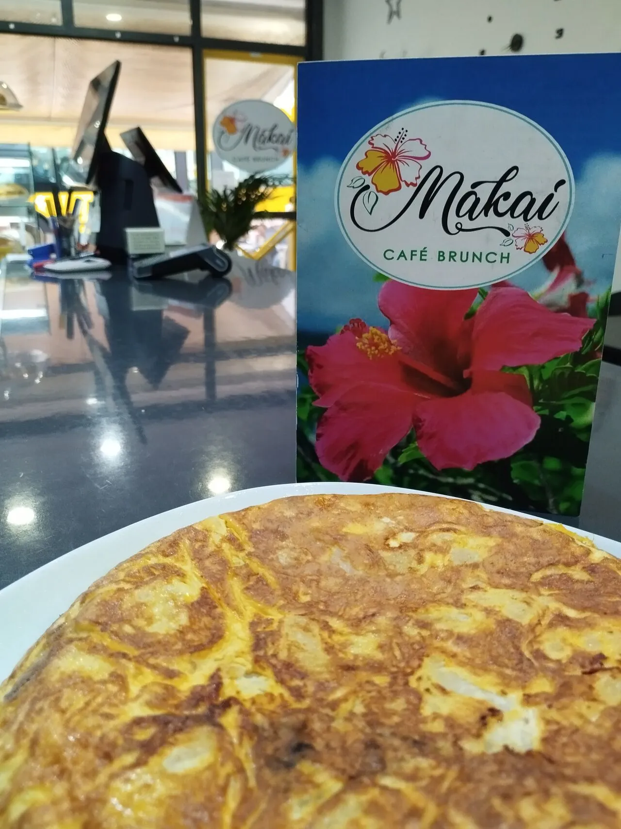 Tortilla española servida en el café Makai, con un menú de brunch visible en el fondo, destacando un ambiente acogedor y moderno.